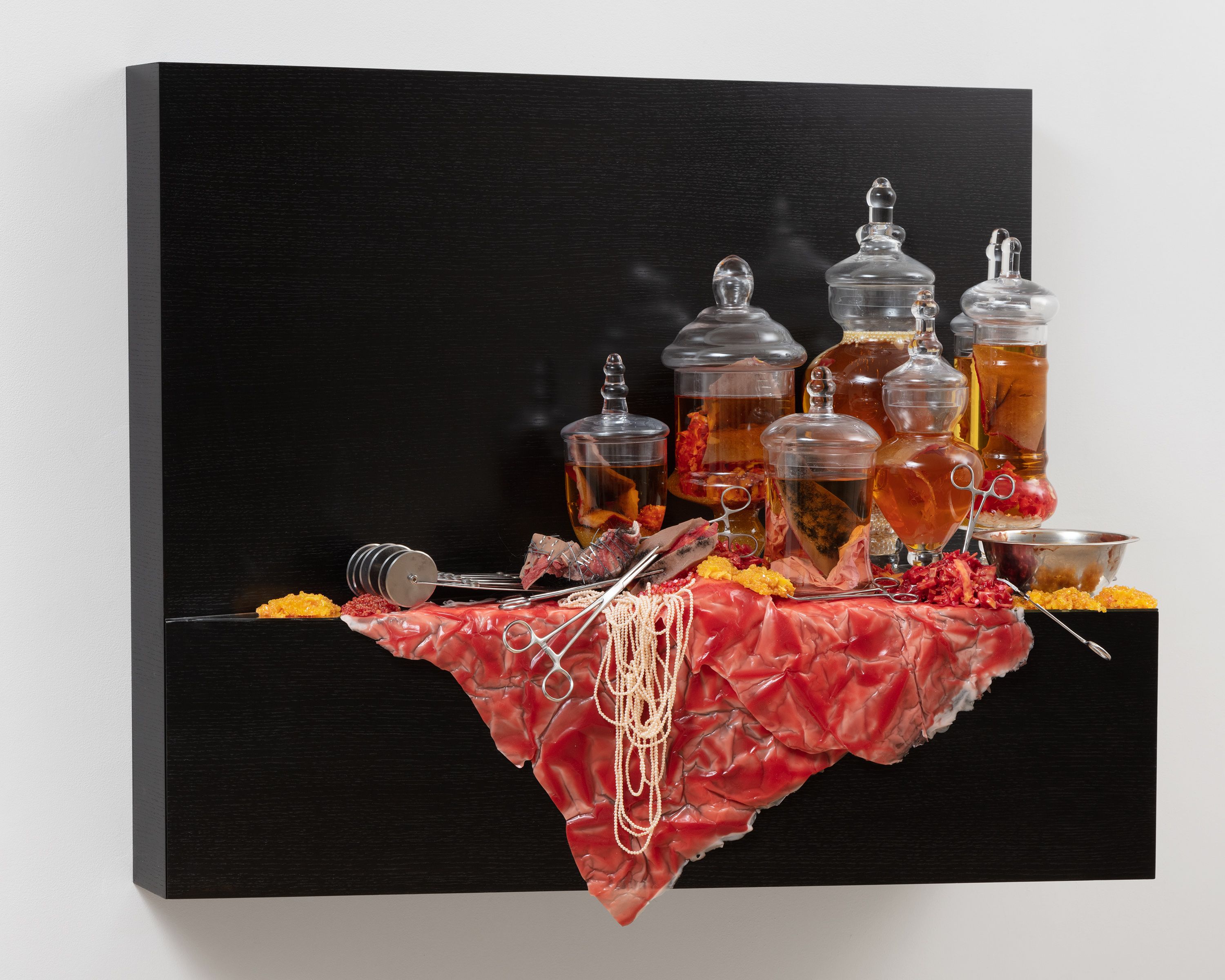 This sculpture is a wooden shelf mounted to wall. The shelf is stained a very dark brown, and is covered in apothecary jars, pearls, surgical equipment, and silicon modeled to look like human flesh. The apothecary jars are filled with whiskey and contain silicon objects that resemble human flesh or body parts.