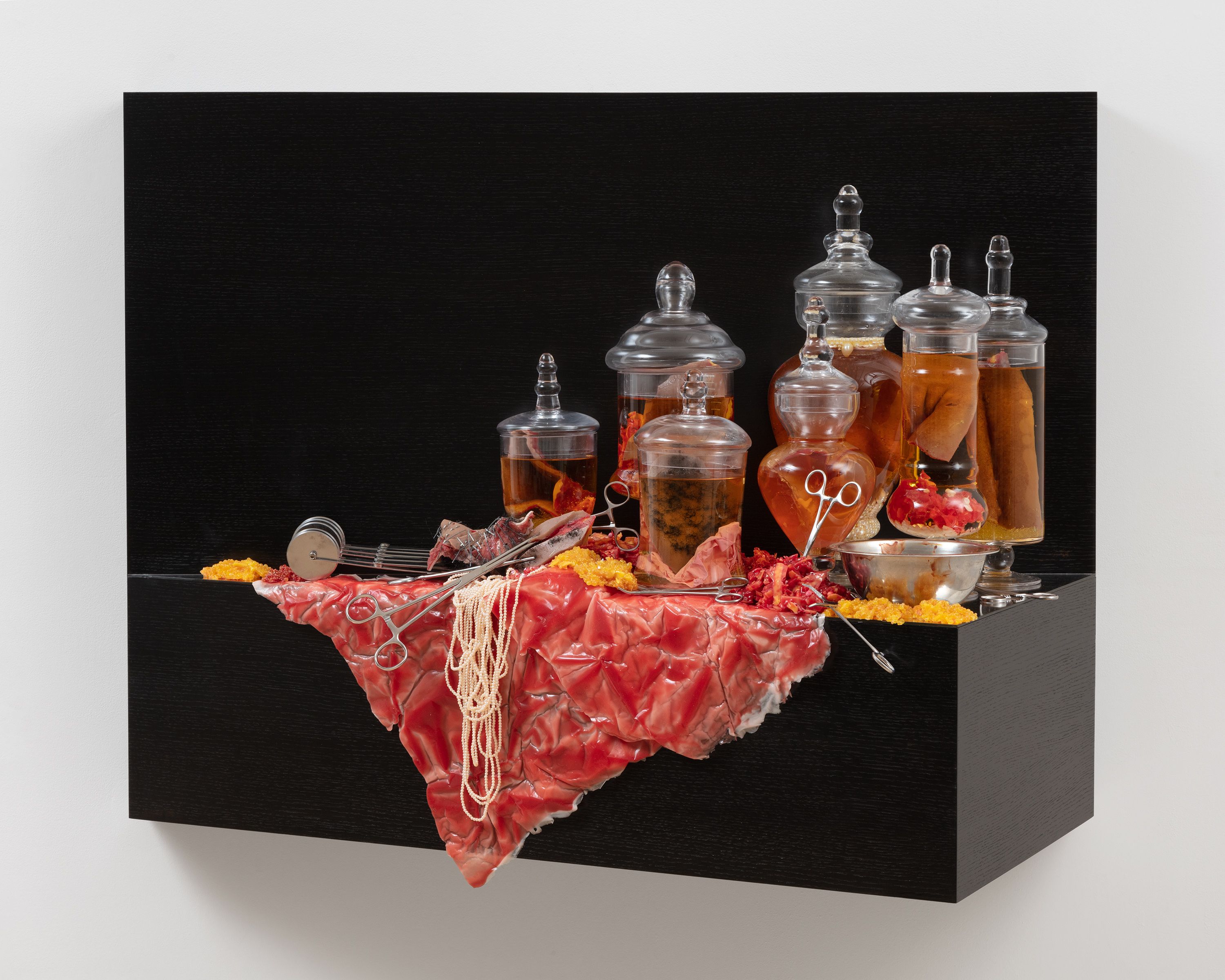 This sculpture is a wooden shelf mounted to wall. The shelf is stained a very dark brown, and is covered in apothecary jars, pearls, surgical equipment, and silicon modeled to look like human flesh. The apothecary jars are filled with whiskey and contain silicon objects that resemble human flesh or body parts.